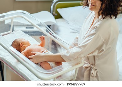 New Born Baby In Maternity Hospital. Selective Focus. Mother Touching And Caressing Her Infant Boy In Cot In Postpartum Ward. Baby Health Care Concept.