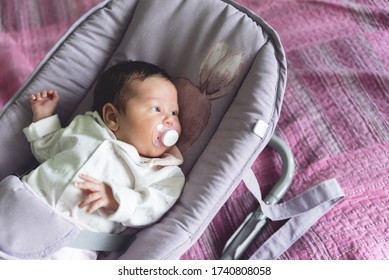 New Born Baby With A Plastic Pacifier In His Mouth Lies Still On A Swing