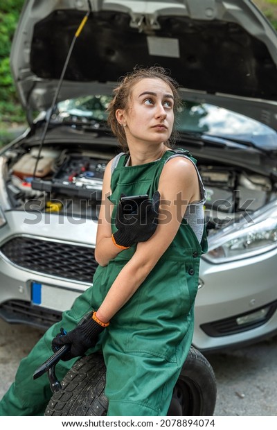 a new broken car is standing on\
the road near the highway near which the girl is a mechanic who\
will repair it. Car repair concept. Woman mechanic\
concept