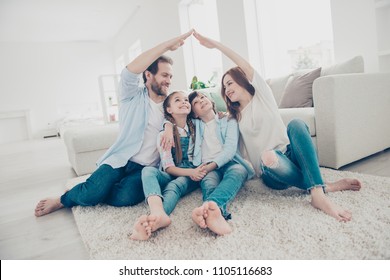 New building residential house purchase apartment concept. Stylish full family with two kids sitting on carpet, mom and dad making roof figure with hands arms over heads