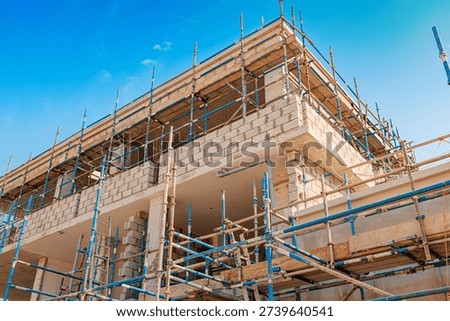 New building structure with masonry block walls and blue scaffolding, illustrating ongoing development and housing projects