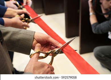 New business venture;  Opening ceremonial red ribbon cutting scissors in hands. Group of people.