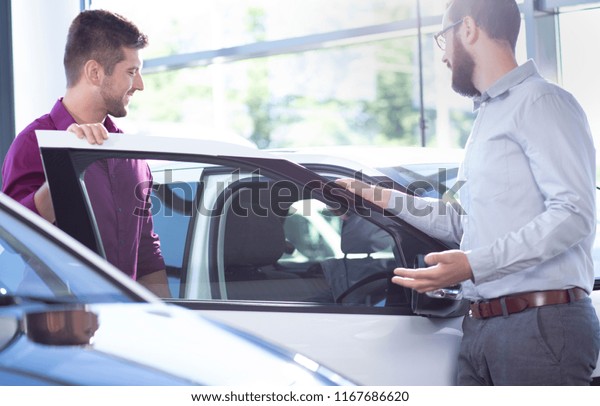 New buyer getting into a car in a showroom. Car\
dealer standing next to a\
car