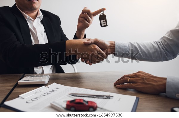 New car buyers and car salesmen are\
shaking hands to make agreements about car\
sales.