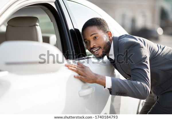 New Car Concept. Black Businessman Checking And\
Touching His New Automobile In Excitement Outside. Selective Focus,\
Copy Space