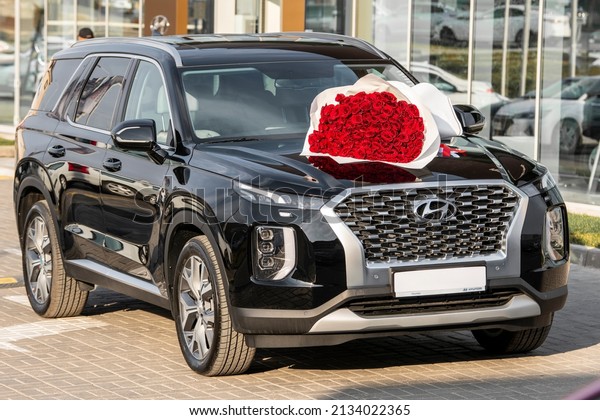 A new car, dark in color, of the Korean brand\
Hyundai is parked in a parking lot near a car dealership. On the\
hood of the car lies a bouquet of red roses. Shymkent, Kazakhstan -\
March 4, 2022