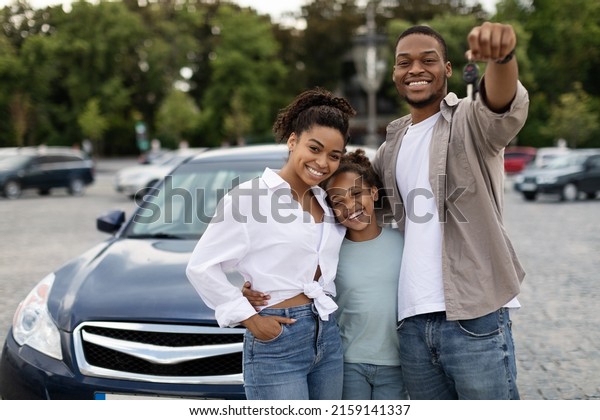 New Car. Happy Black\
Family Showing Own Automobile Key To Camera Standing Near Auto\
Posing Outdoor. Vehicle Purchase And Rent, Dealership Advertisement\
Concept