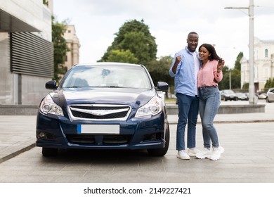 New Car. Happy Black Woman Showing Automobile Keys, Man Embracing Wife Shaking Clenched Fists, Young Family Celebrating Buying New Car In Dealership Center, Using Auto Rental Service, Full Body Length