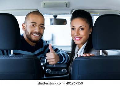 New Car New Life. Shot Taken From A Backseat Of The Car Happy Loving African Couple Smiling To The Camera Over Their Shoulders While Sitting In A Car Man Showing Thumbs Up