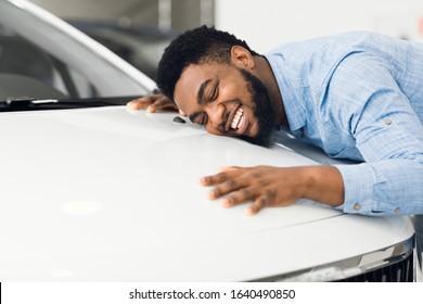 New Car Owner. Happy African American Man Touching Hugging His Brand-New Auto Cherfully Buying Vehicle In Auto Dealership. Selective Focus