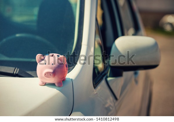 New car with pink piggy money bank on the\
hood, outdoors sunny background. Dealership offering credit finance\
services. Auto leasing, vehicle purchase concept. Economic success,\
property insurance.