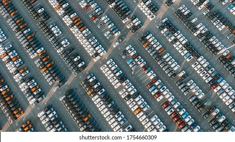 New cars of different colors stand in even rows in a giant park at a car factory at sunset, aerial view