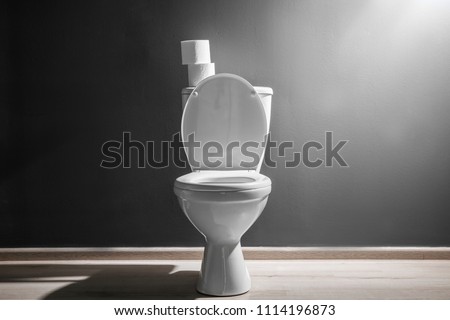 New ceramic toilet bowl near grey wall, side light