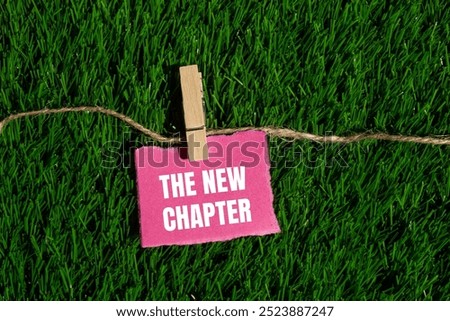 The new chapter message written on ripped torn pink paper piece with green grass background. Conceptual the new chapter symbol. Copy space.