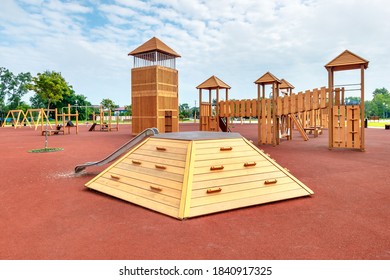 The New Child Playground With Yellow Wooden Equipments And Red Poured In Place Rubber Surface.