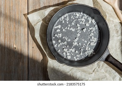 New Clean Cast Iron Pan With Salt On A Wooden Table On Parchment. Background With Cooking Utensils And Kitchen Utensils For Frying. Caring For Cast Iron Cookware