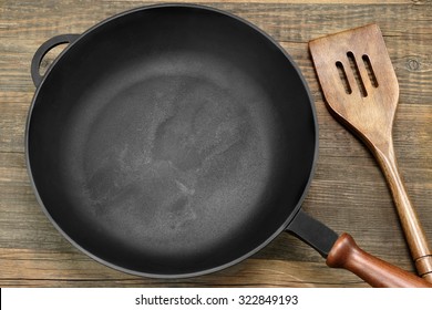 New Clean Empty Cast Iron Frying Pan And Spatula Overhead View On The Wood Background