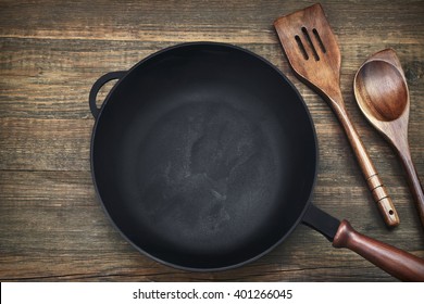 New Clean Empty Cast Iron Frying Pan And Spatula Top View On The Wooden Background