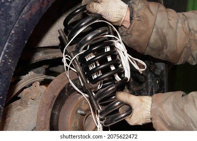 New Coil Spring In Hands On Broken Car On Bottle Hydraulic Jack Background - Vehicle Suspension Repair In Garage