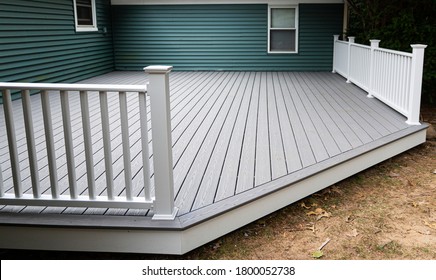 New composite deck on the back of a house with green vinyl siding.with whie railings.