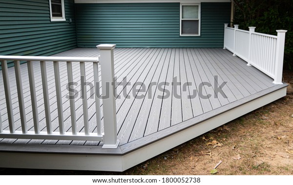 New composite deck on the back of a house\
with green vinyl siding.with whie\
railings.