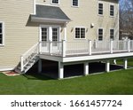 New composite deck. White veranda and railing posts, brown boards, elevated above ground. Showing support frame and gravel under porch.