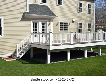 New composite deck. White veranda and railing posts, brown boards, elevated above ground. Showing support frame and gravel under porch. - Shutterstock ID 1661457724