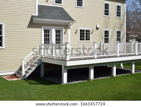 New composite deck. White veranda and railing posts, brown boards, elevated above ground. Showing support frame and gravel under porch.