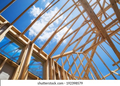 New construction home framing against blue sky, closeup of ceiling frame.