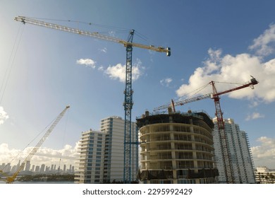 New construction site of developing residense in american urban area. Industrial tower lifting cranes in Miami, Florida. Concept of housing growth in the USA
