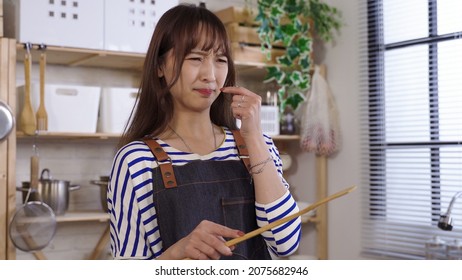 New To Cooking. Closeup Korean Lady Making A Grimace Embarrassedly After Tasting The Dish With The Finger. Genuine Lifestyle