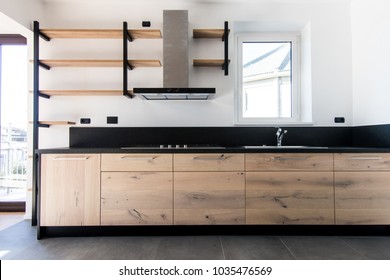 Die neue Küche aus Holz, Edelstahl und schwarzem Granit ist in einem neuen Apartment eingerichtet. Innenausstattung mit freiliegenden Regalen und dunkelgrauem Boden. Eichenholz, schwarze Farbe und Inox-Stahl
