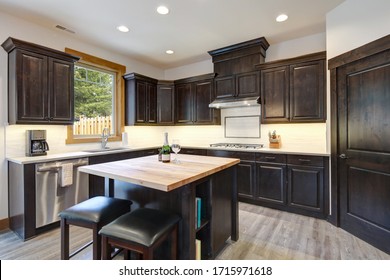 New dark brown wooden kitchen interior with light grey hardwood with white tile backsplash and small wooden island with two stools.