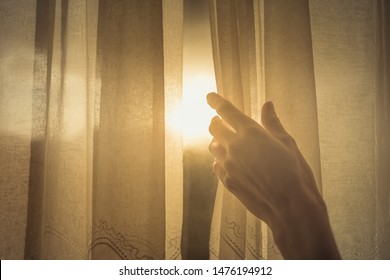 New Day And New Beginnings, Rise And Shine Concept. Hand Opening Up Window Curtain Letting The Early Morning Sunshine In. 