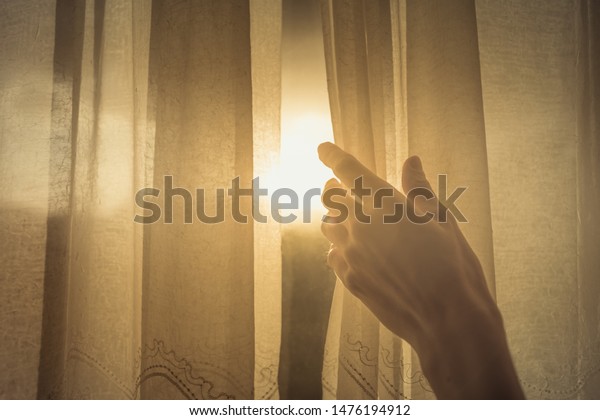 New day and new beginnings, rise and shine concept. Hand\
opening up window curtain letting the early morning sunshine in.\
