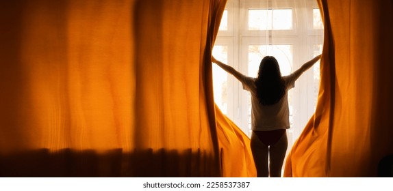 New day. Silhouette of woman opening orange curtains in morning at window. Web banner with copy space. Rear view. Concept of freedom, hope and happiness. - Powered by Shutterstock