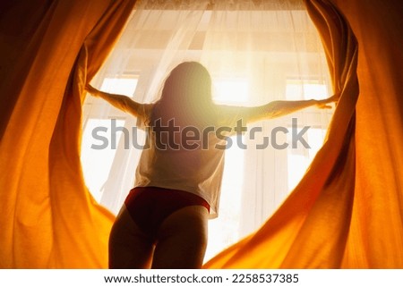 New day. Silhouette of woman opening orange curtains in morning at window. Bottom view. Concept of freedom, hope and happiness.