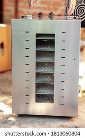 New Dehydrating Machine Standing On The Ground, Woman Hands Unpacking It. Equipment For Producing Dry Meat Or Vegetarian Jerky. Metal Door, Many Shelves Inside.