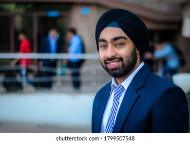 New Delhi, Delhi, India - 12/05/2014: A Sikh Indian boy wearing a turban smiles while taking a walk in the college campus. A bearded university student in formal wear with blurred background.