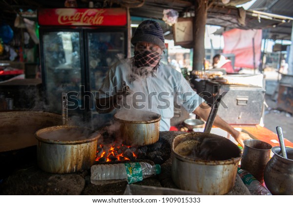 New Delhi, India - 6\
January 2021: Man cooking tea Indian style Hot Milk tea on coal\
powered clay stove (earthen chulha, as usually called in India) ,\
Chai stall.