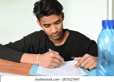 New Delhi, India. December 12,2020. Young Male University Student Studying Preparing Offline For Exams Writing Complete Notes In Notebook Sitting At Desk Chair At Home Doing Homework.