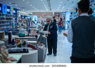 New Delhi, India- Jan 7 2020: A Woman In A Shoes Showroom, Shopping For Shoes, Sitting Down While A Male Shop Assistant Hands A Shoe To Her To Try On 