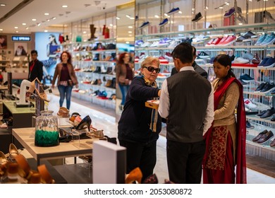 New Delhi, India- Jan 7 2020: A Woman In A Shoes Showroom, Shopping For Shoes, Sitting Down While A Male Shop Assistant Hands A Shoe To Her To Try On 