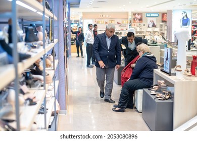 New Delhi, India- Jan 7 2020: A Woman In A Shoes Showroom, Shopping For Shoes, Sitting Down While A Male Shop Assistant Hands A Shoe To Her To Try On 