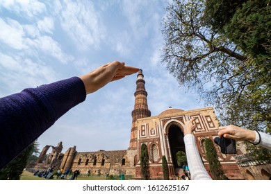 New Delhi, India - January 5, 2020: Tourists attempt to take forced perspective photos of the Qutub Minar ancient pillar and ruins - Shutterstock ID 1612625167