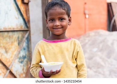 New Delhi, India - June 23, 2019: A Poor Young Kid Smiling And Holding A Bowl Of Food In His Hand.