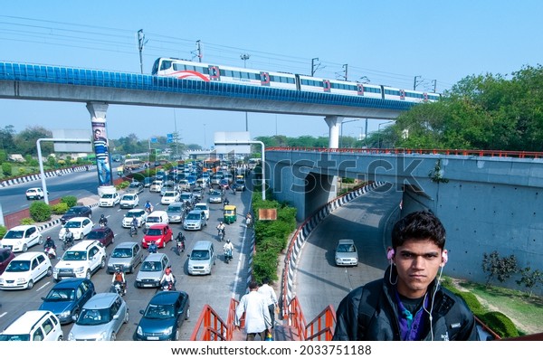 New Delhi, India-March 15 2020: young boy rushing\
to college while listening music walking on foot over bridge at\
dhaula kuan in Delhi, heavy traffic and Airport metro crossing ring\
road,