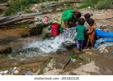 New Delhi, India-Sep 29 2021: woman wringing out clothes while cleaning with waste water, water drainage by Pipe in to drain. children playing with water near Indraprastha Estate in Capital of India.