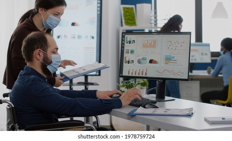 New Disabled Paralysed Invalid Employee Company Staff Member With Face Mask Look At Computer Asking About Corporate App Program Software, Manager Helping His Working In New Normal Business Office