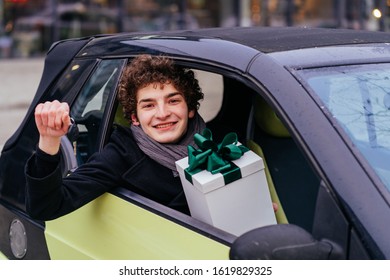 New Driver. Young Curly Caucasian Man Buy First Used Car. Happy Eaxcited Male Teenager Student Holding Key And Box Gift With Green Bow Sitting In His New Car.